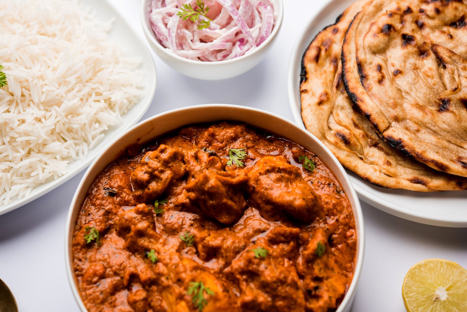 Murgh Makhani or Butter chicken tikka masala served with roti or Paratha and plain rice along with onion salad in terracotta crockery. selective focus